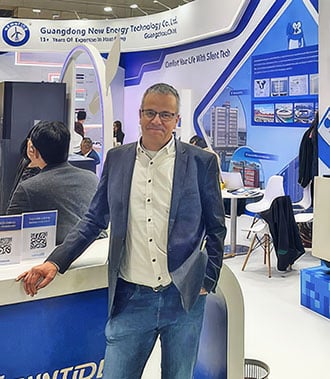 Stephan Holzwart am Messestand von Newntide (Guangdong New Energy Technology) auf einer Fachmesse, gekleidet in Sakko, Hemd und Jeans, lächelnd in die Kamera blickend.